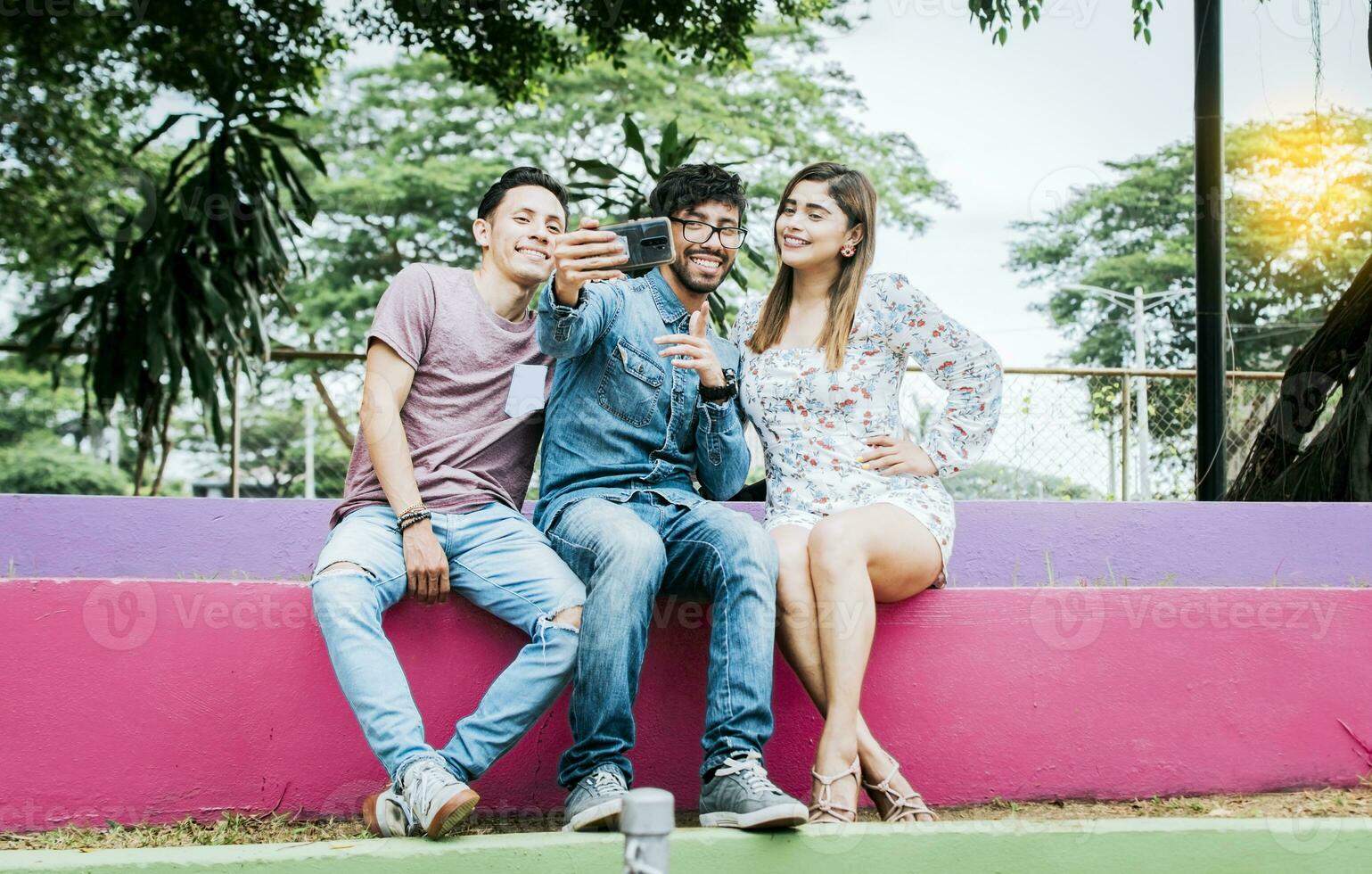 estilo de vida do três amigos sentado dentro uma parque levando uma selfie, três Adolescência amigos sentado dentro uma parque levando selfies. encontro do três feliz amigos levando uma selfie sentado dentro a parque foto