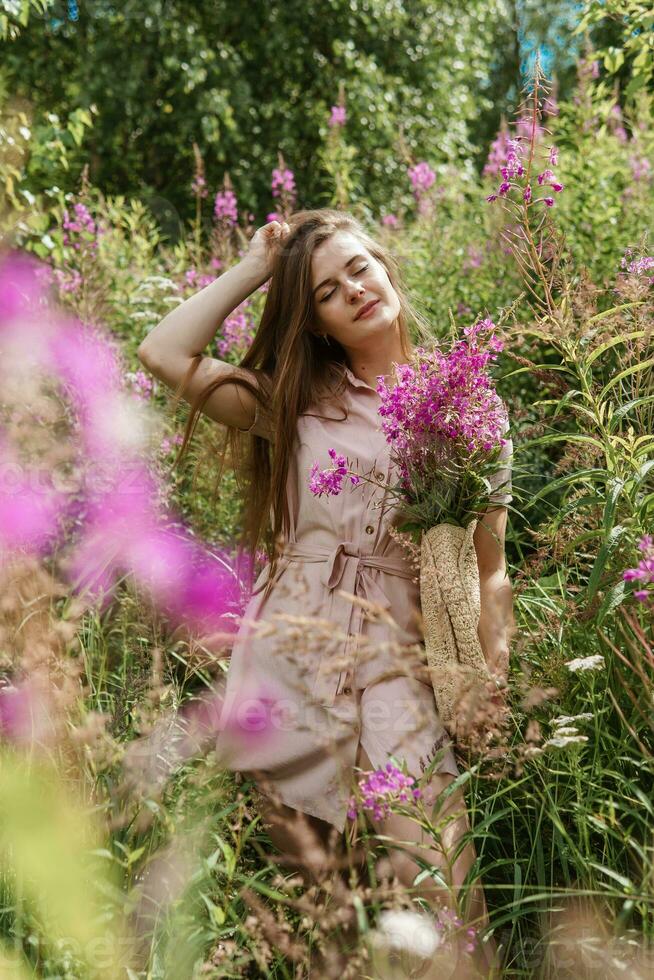 jovem mulher dentro natureza com uma ramalhete do Rosa selvagem flores uma ramalhete do ivan-chá dentro a mãos do uma mulher. foto