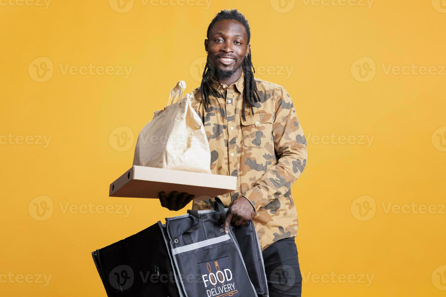 retrato do restaurante trabalhador segurando papel saco entregando Leve embora Comida para clientes durante almoço tempo. africano americano entregador carregando térmico mochila cheio com velozes Comida dentro estúdio foto