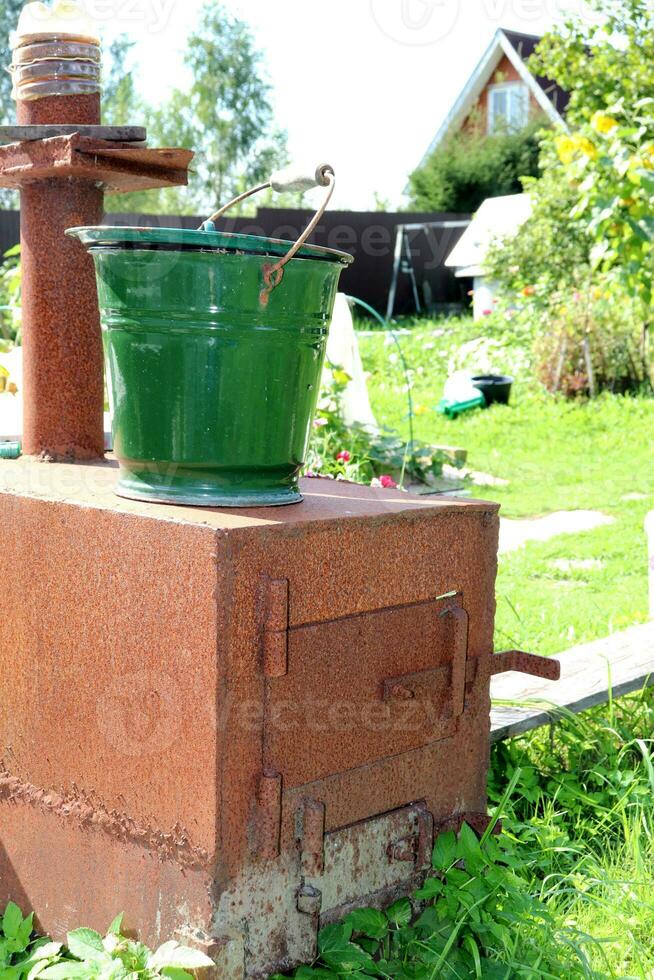 uma metal balde carrinhos em uma caseiro ferro fundido fogão dentro a vegetal jardim do uma Vila casa. vertical foto, fechar-se foto