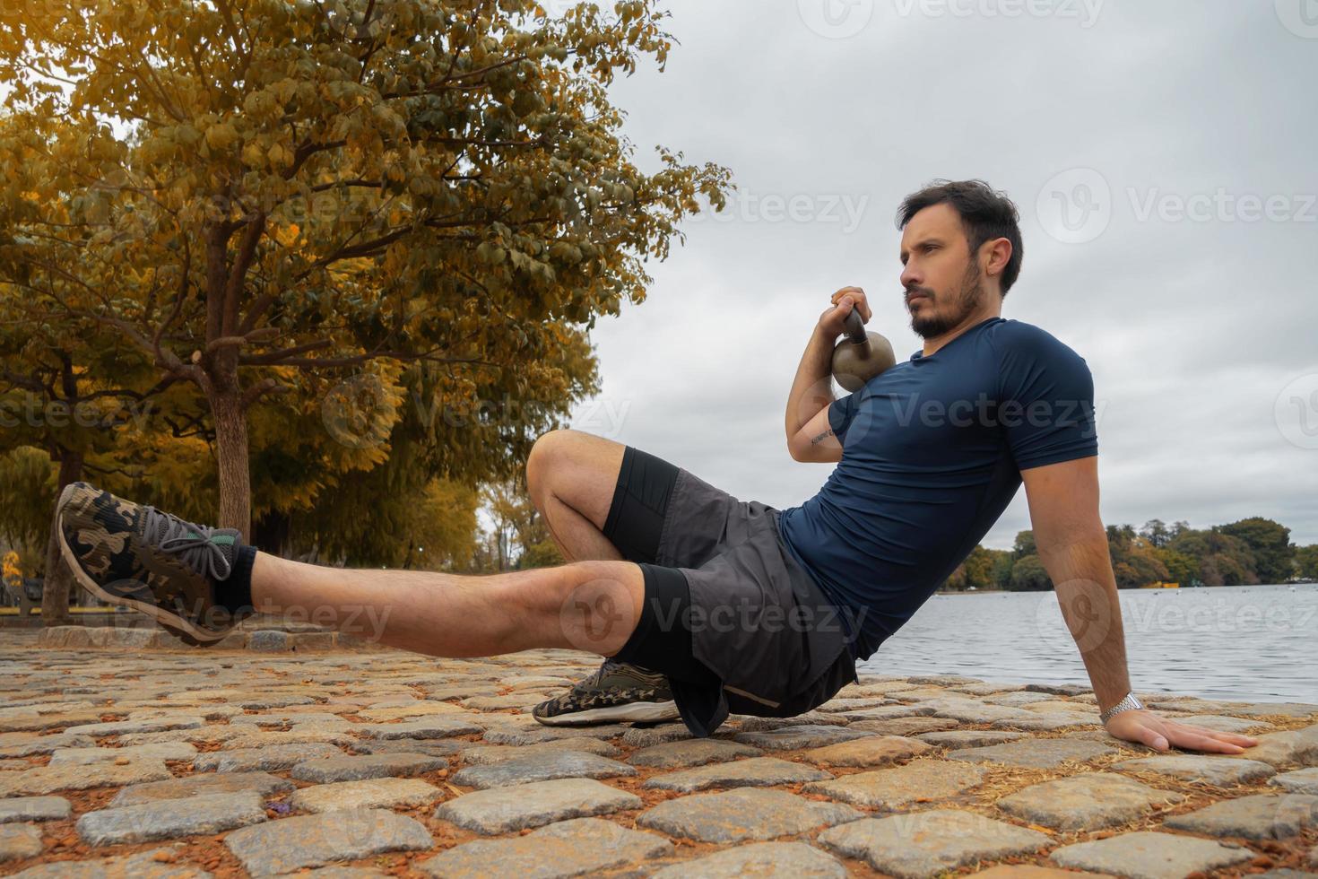 instrutor de fitness masculino construindo músculos com chaleira no parque foto