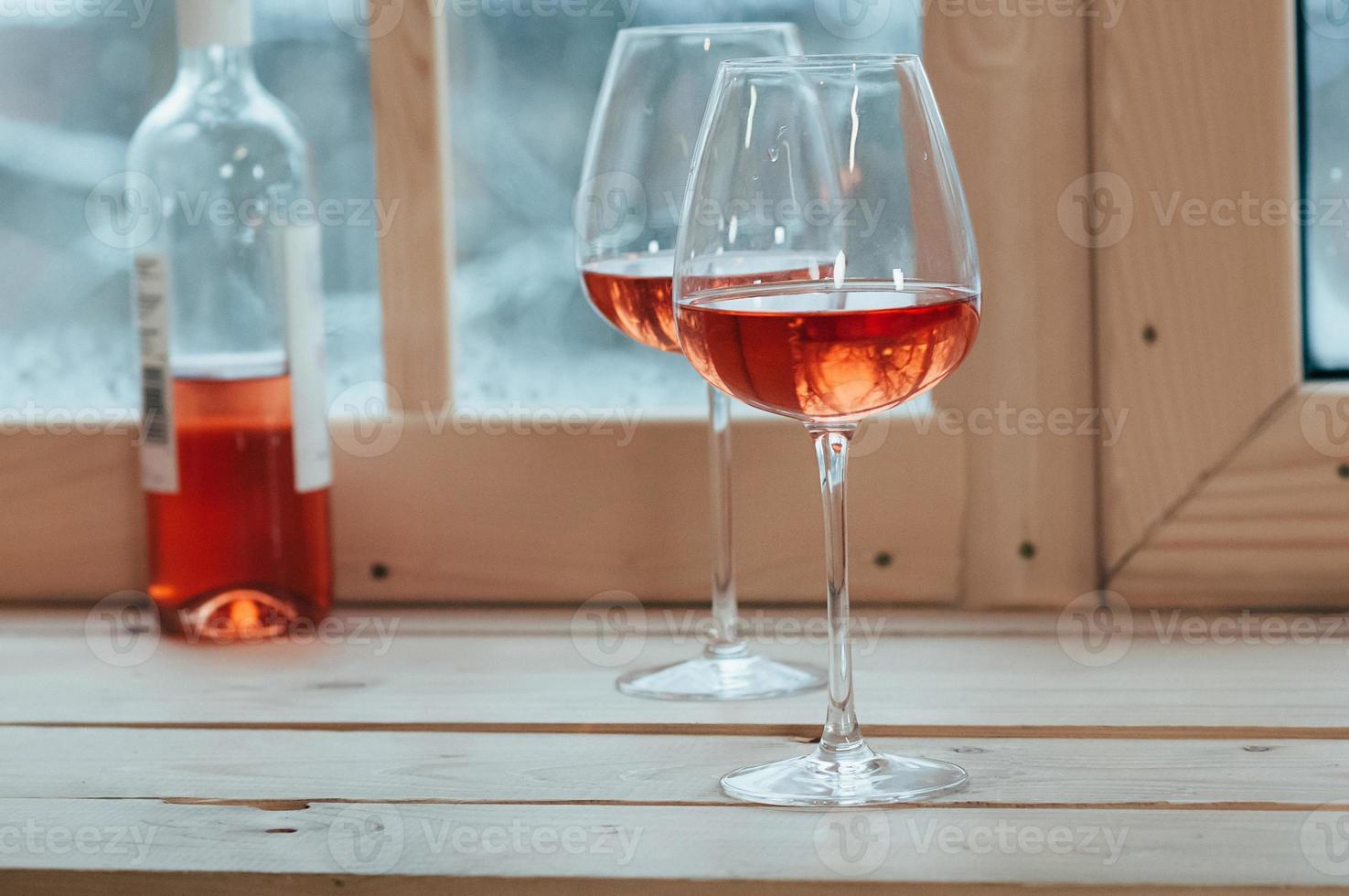 garrafa de vinho rosé e duas taças no parapeito da janela foto