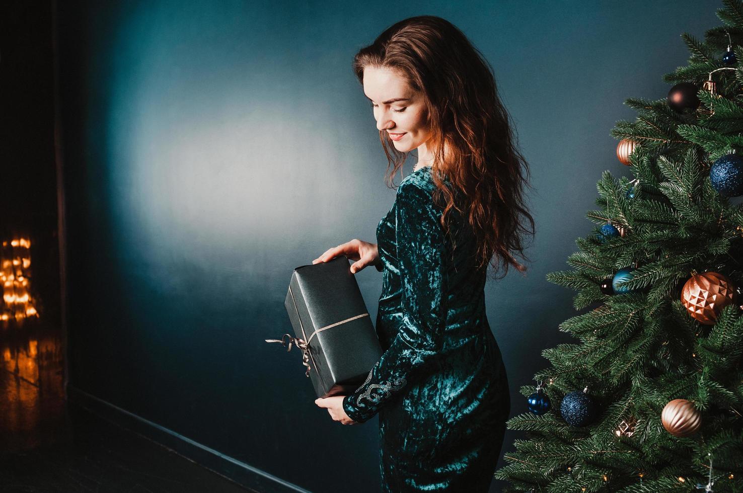 linda garota segurando uma caixa de presente perto da árvore de natal foto