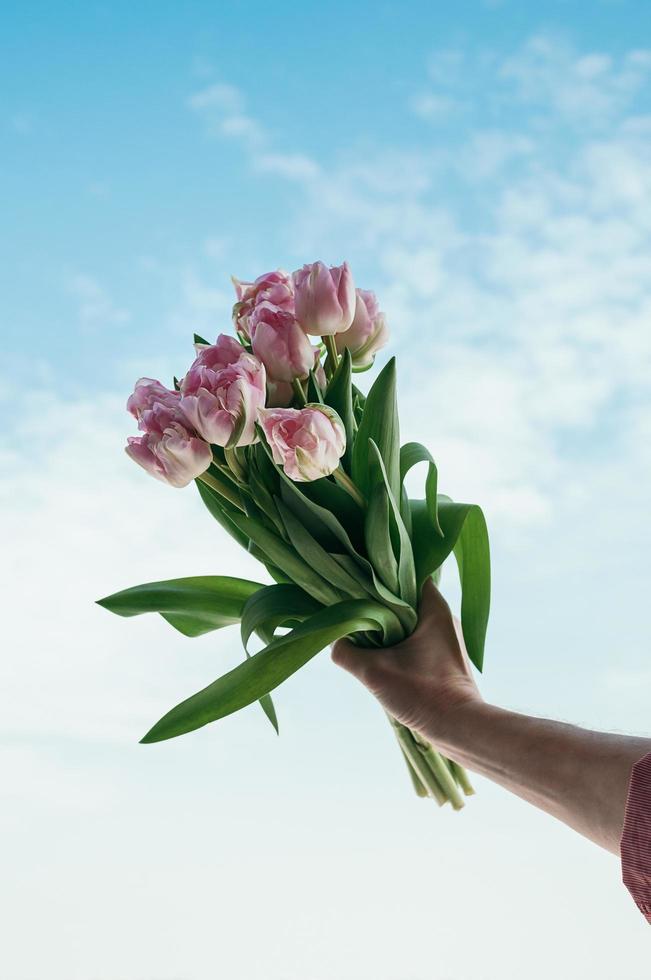 buquê de flores rosa na mão contra o fundo do céu azul foto