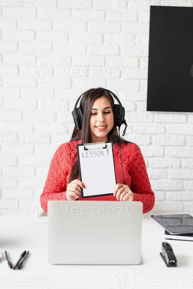 jovem latina com fones de ouvido pretos ensinando inglês online foto