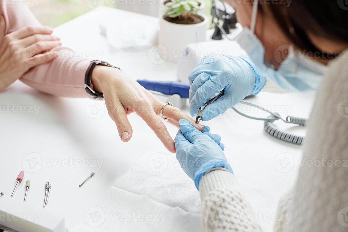 mestre de manicure usando pinças para fazer manicure para uma cliente foto