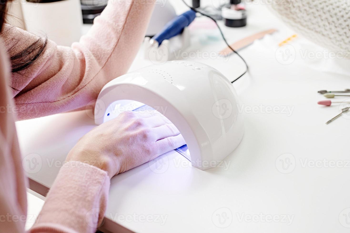 mulher no salão de manicure secando as unhas em uma lâmpada ultravioleta foto