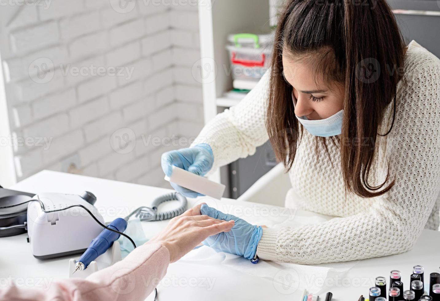 manicure mestre em máscara e unhas com luvas de uma cliente foto