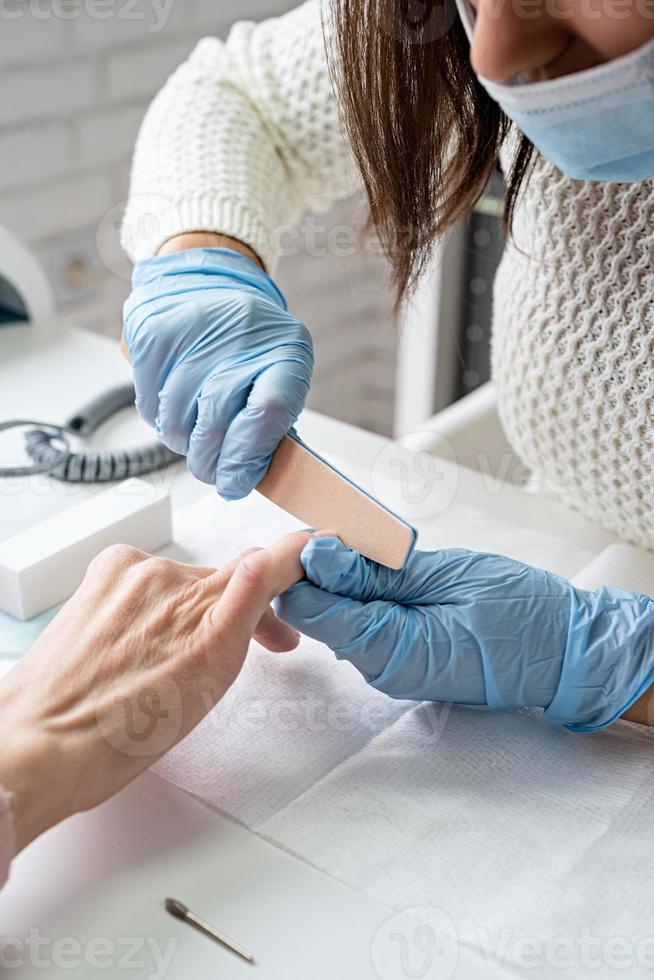 Mestre de manicure usando lixa de unha para polir a unha de uma cliente foto