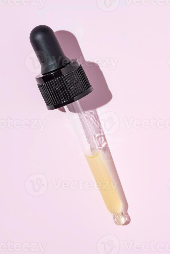 conta-gotas de pipeta de garrafa e retinol líquido amarelo-alaranjado ou gel ou soro de vitamina c em um fundo rosa foto