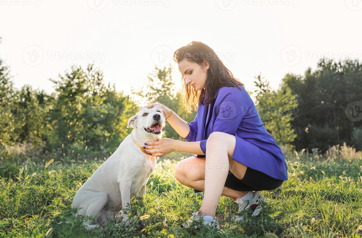 jovem mulher atraente abraçando seu cachorro no parque ao pôr do sol foto