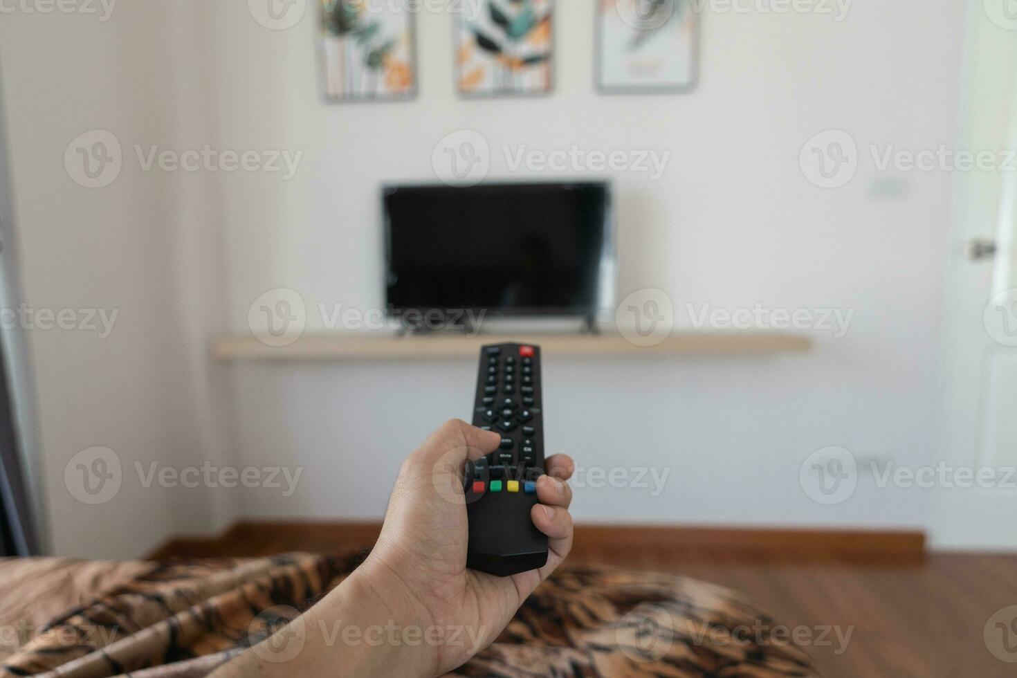 fechar acima televisão controlo remoto ao controle dentro mão homem apontando para televisão conjunto e girando isto em ou desligado. selecionar canal assistindo televisão às casa dentro a vivo quarto relaxar. foto