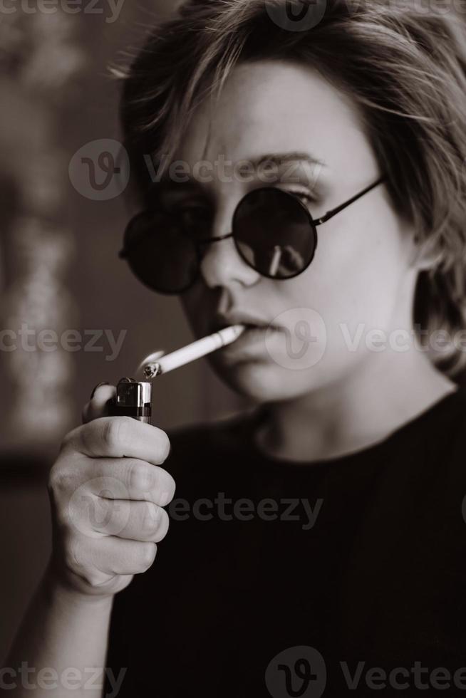 garota com cabelo curto e óculos de sol no espelho fumando cigarro foto
