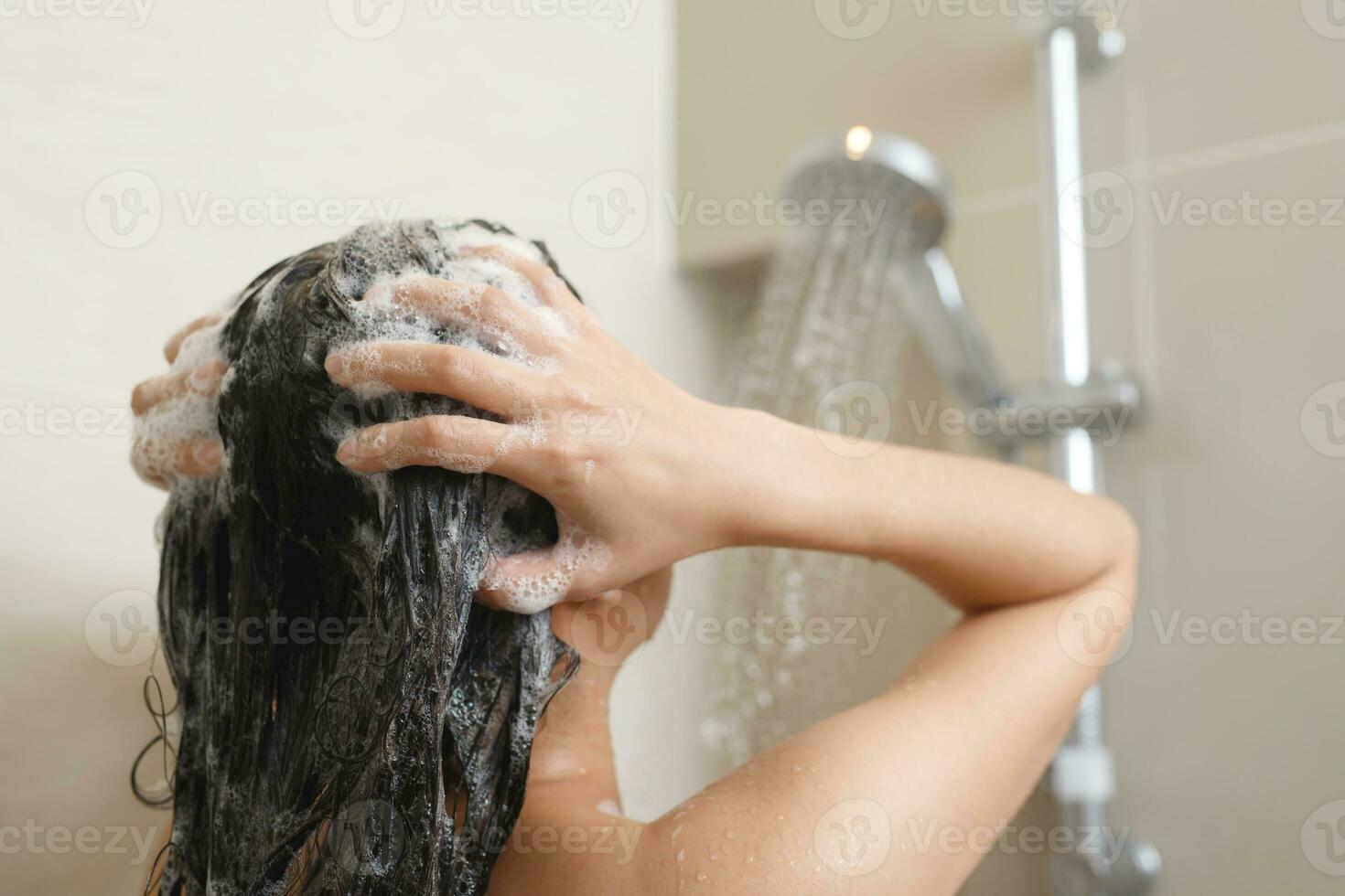 mulher levando chuveiro e lavando cabelo com xampu foto