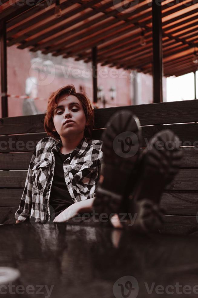 jovem mulher com cabelo ruivo curto em um bar coloca as pernas na mesa foto