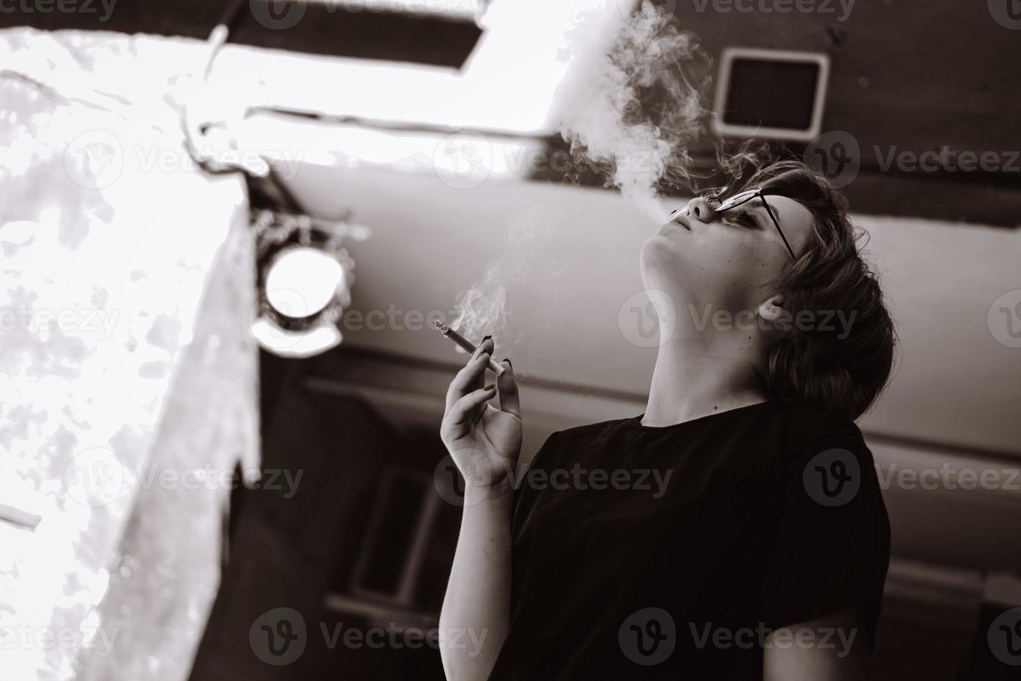 garota com cabelo curto e óculos de sol no espelho fumando cigarro foto