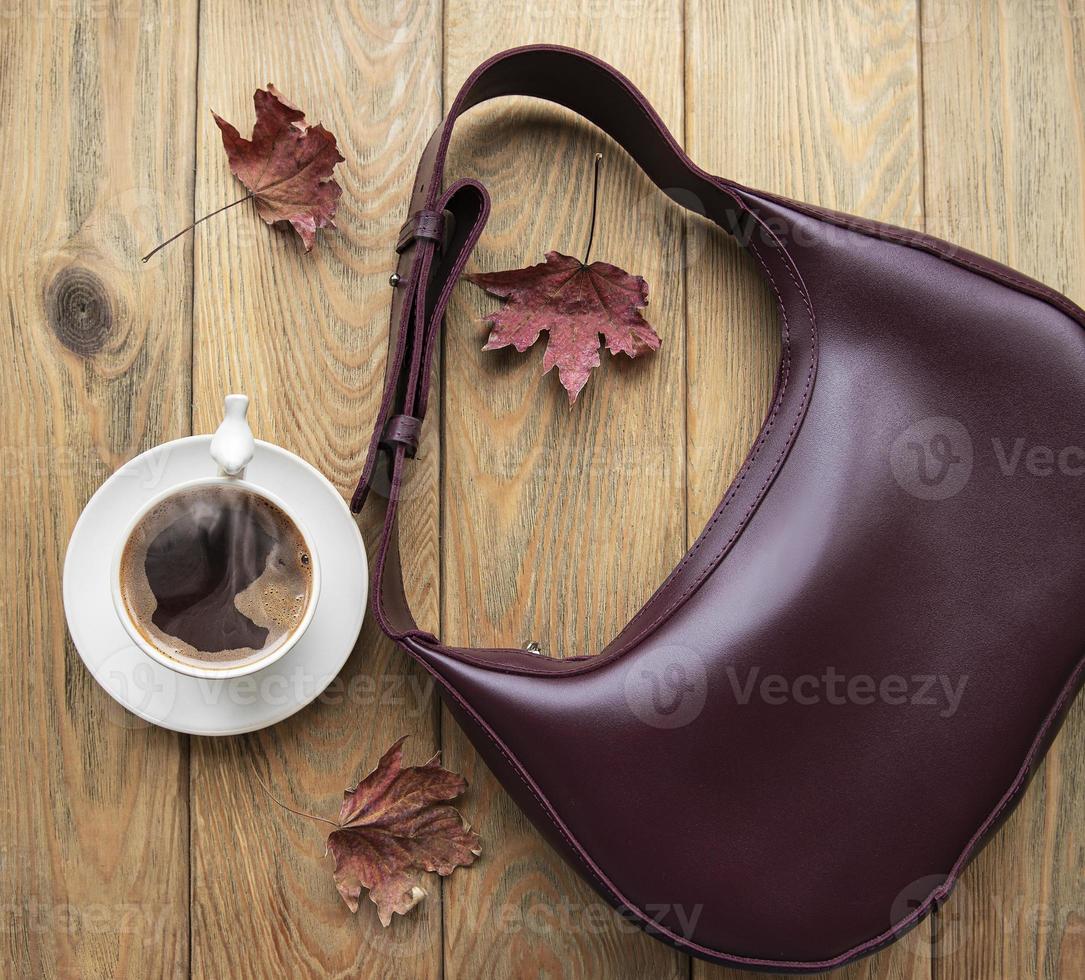 bolsa de couro, xícara de café e folhas de outono em um fundo de madeira foto