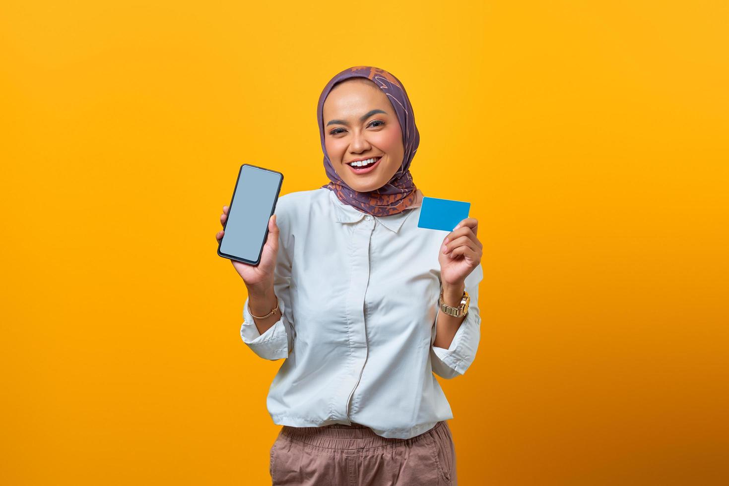 alegre mulher asiática segurando um smartphone e um cartão em branco foto