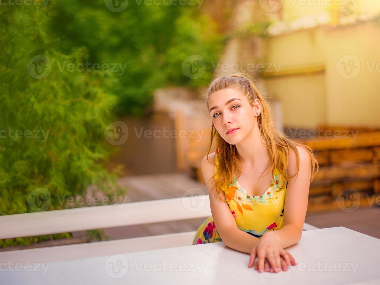 loira garota está sentada em uma mesa vazia de um café de rua. foto