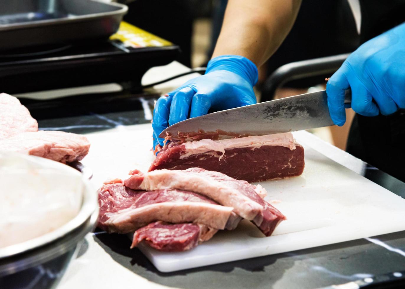 chef corta carne crua com uma faca em uma tábua, cozinheiro corta carne crua foto