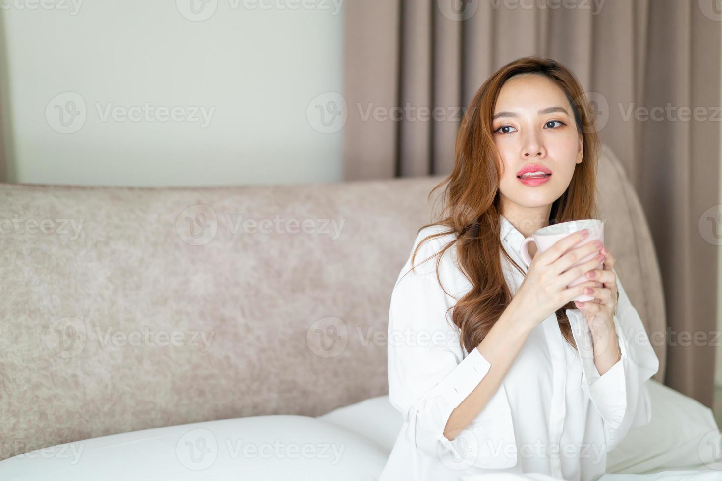 retrato de mulher bonita acordar e segurando uma xícara de café ou caneca na cama foto