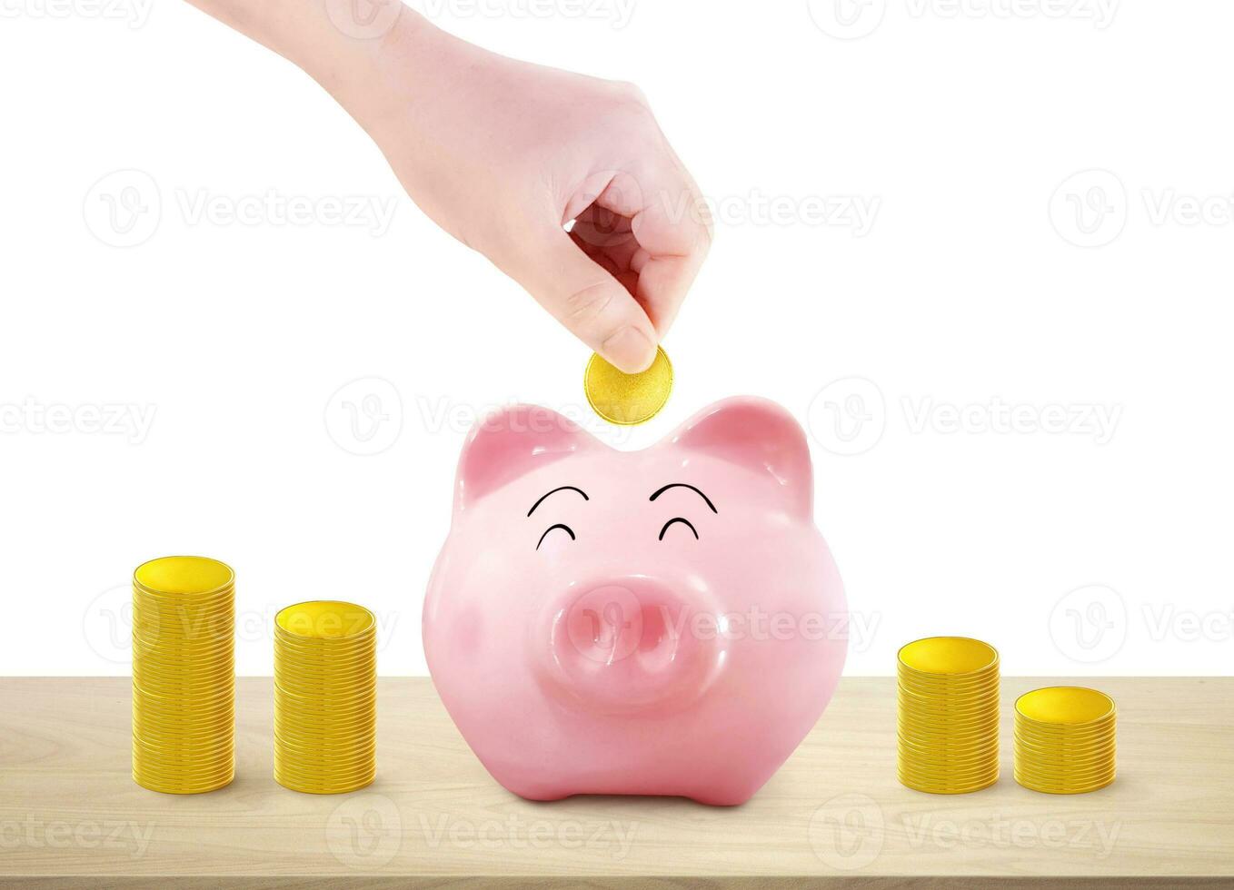 mão coloca ouro moedas para dentro uma porquinho banco e uma pilha do ouro moedas em uma de madeira mesa. branco fundo foto