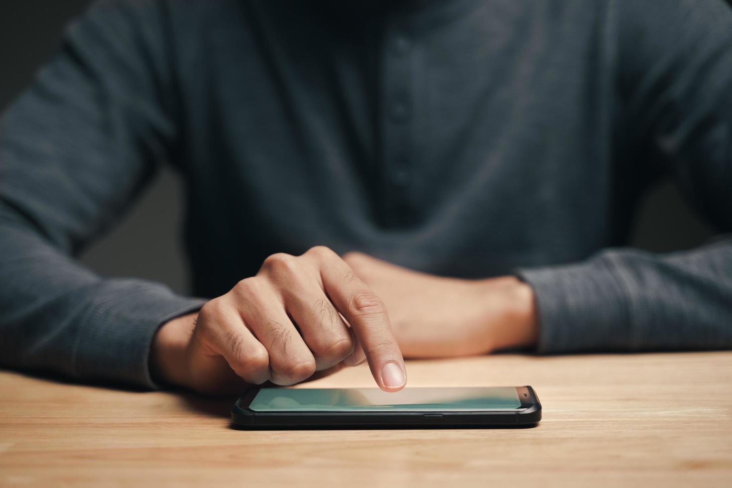 homem usando um smartphone na mesa de madeira, pesquisando, navegando foto