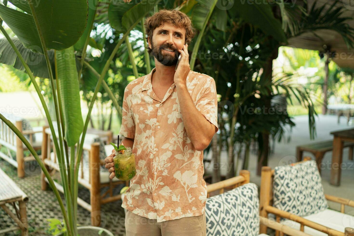 bonito homem com barba posando dentro cafeteria com tropical interior e falando celular telefone. foto