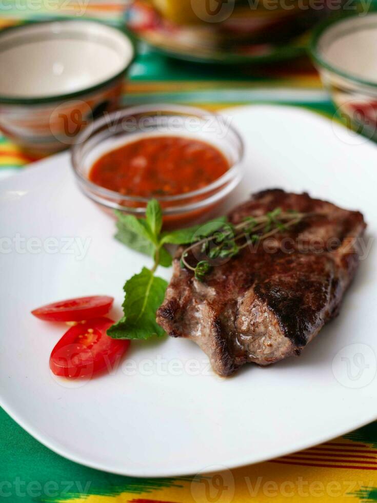 carne bife com tomate molho, tomates e ervas dentro oriental estilo em uma mesa com uma chaleira e uma copo para chá. foto