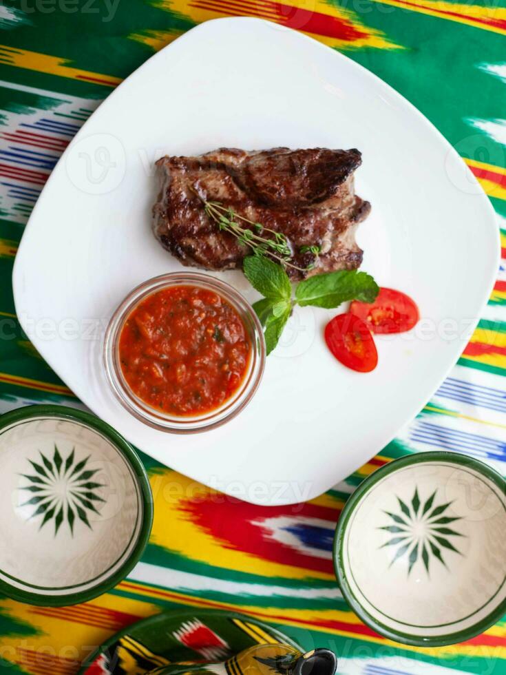 carne bife com tomate molho, tomates e ervas dentro oriental estilo em uma mesa com uma chaleira e uma copo para chá. foto