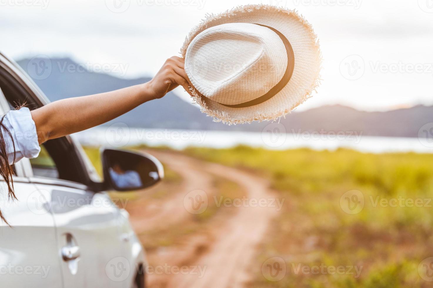 mão de uma mulher feliz segurando um chapéu do lado de fora do carro com janela aberta foto