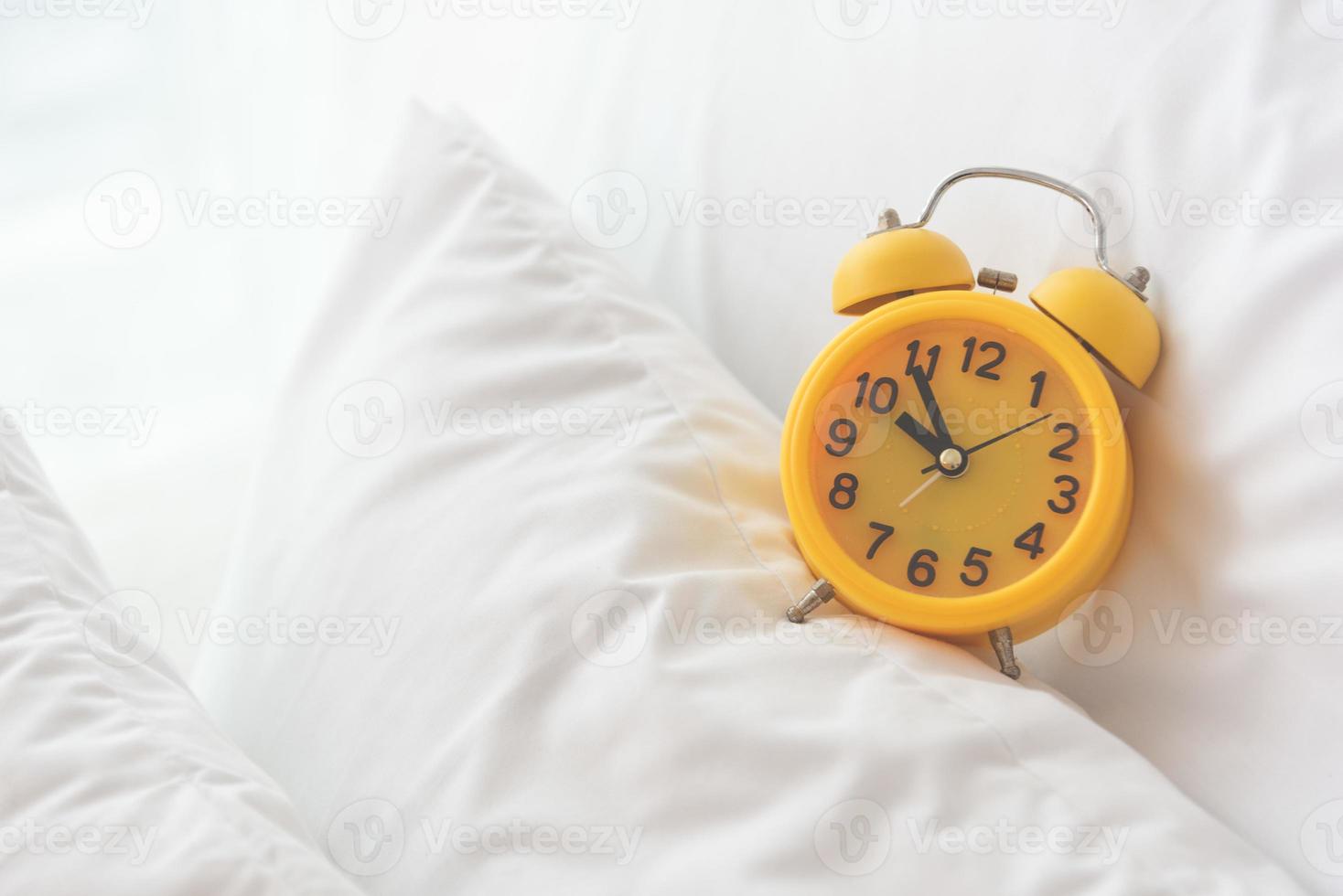 despertador amarelo no fundo branco da cama foto
