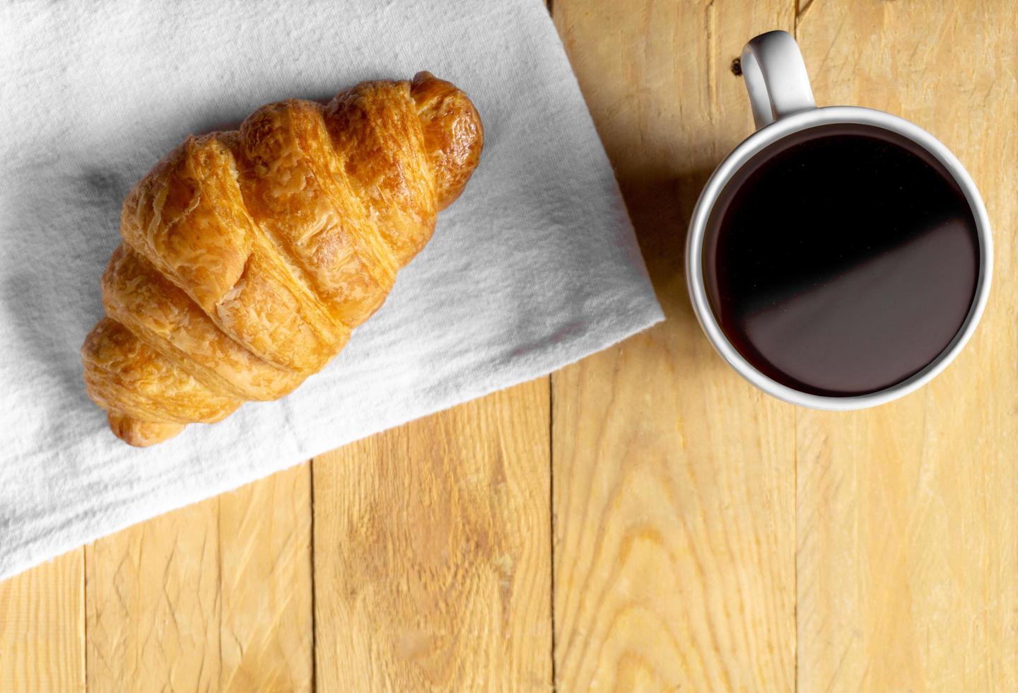 croissant em tecido branco com café na mesa de madeira foto