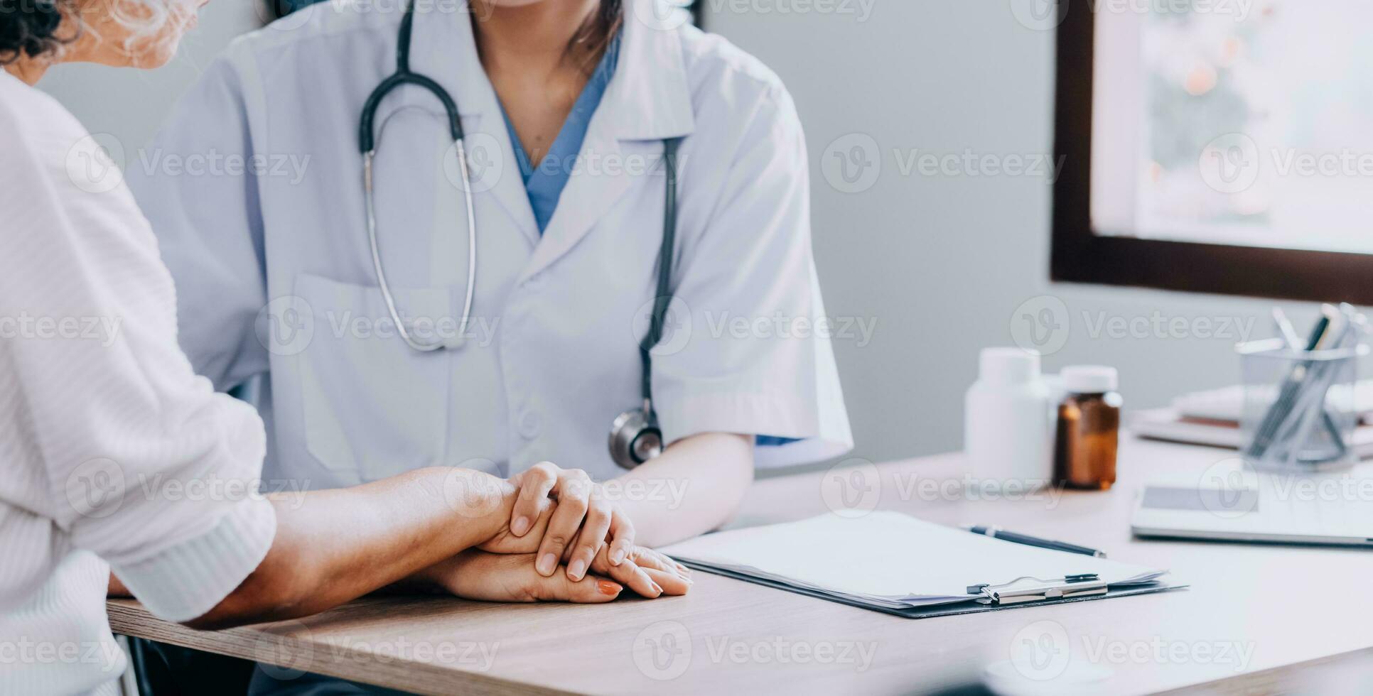 médico dando ter esperança. fechar acima tiro do jovem fêmea médico inclinado frente para sorridente idosos senhora paciente segurando dela mão dentro Palmeiras. mulher zelador dentro branco casaco apoiando encorajando velho pessoa foto