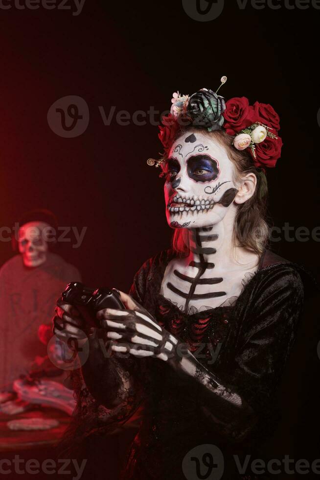 senhora do morte jogando conectados vídeo jogos com controle de video game em console, vestindo crânio faço acima e tradicional santa muerte fantasia. mulher desfrutando jogos concorrência em dia do a morto. foto