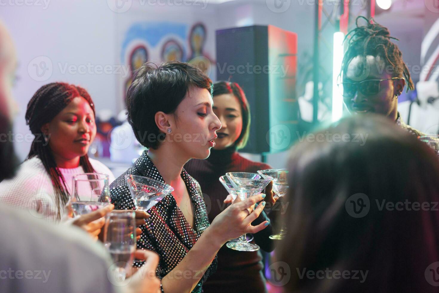 jovem mulher dizendo torrada enquanto bebendo álcool com amigos e a comemorar dentro Boate. clubbers segurando bebida copos, festa e relaxante às discoteca encontro dentro clube foto