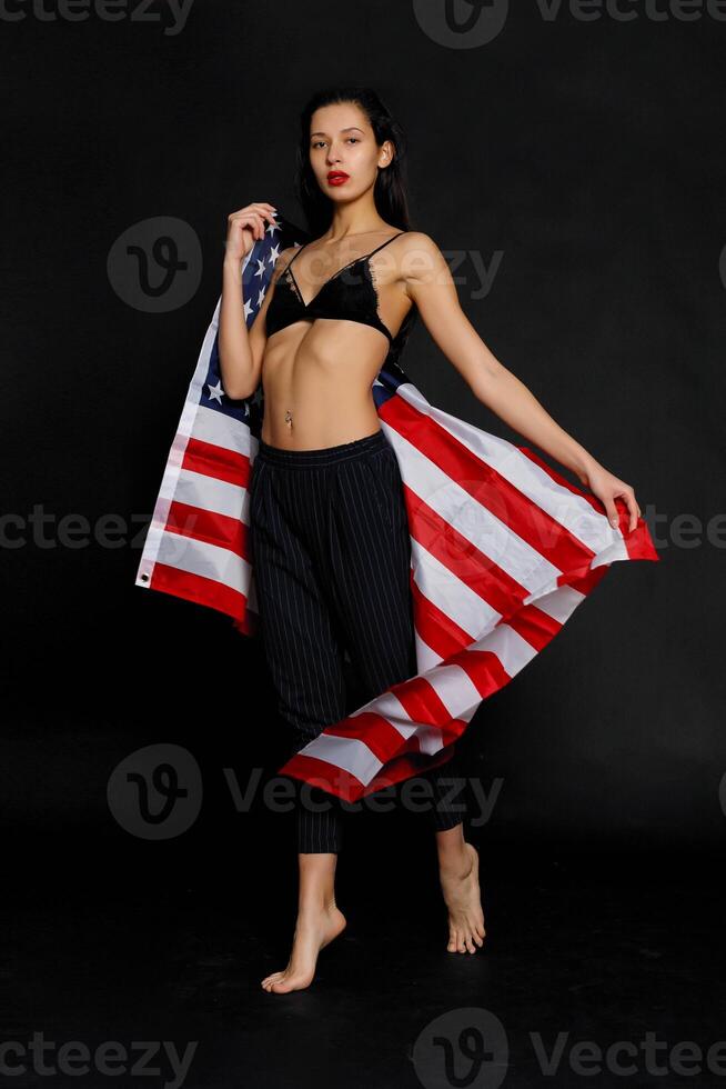 retrato fêmea atleta embrulhado dentro americano bandeira contra Preto fundo foto