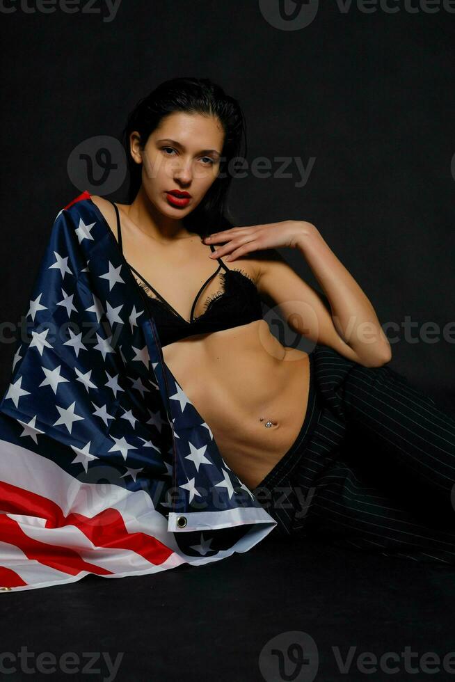 retrato fêmea atleta embrulhado dentro americano bandeira contra Preto fundo foto