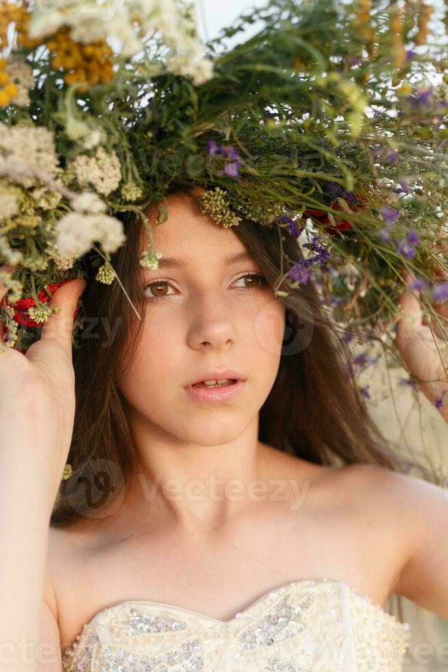 lindo mulher com uma guirlanda em dela cabeça sentado dentro uma campo dentro flores foto
