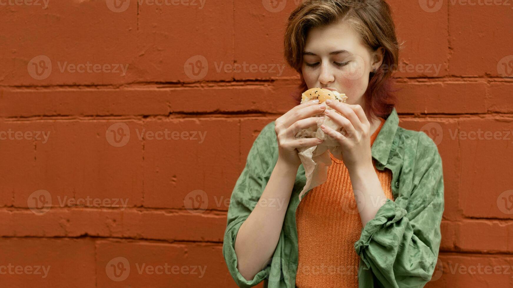 caucasiano jovem mulher comendo hamburguer fora. foto