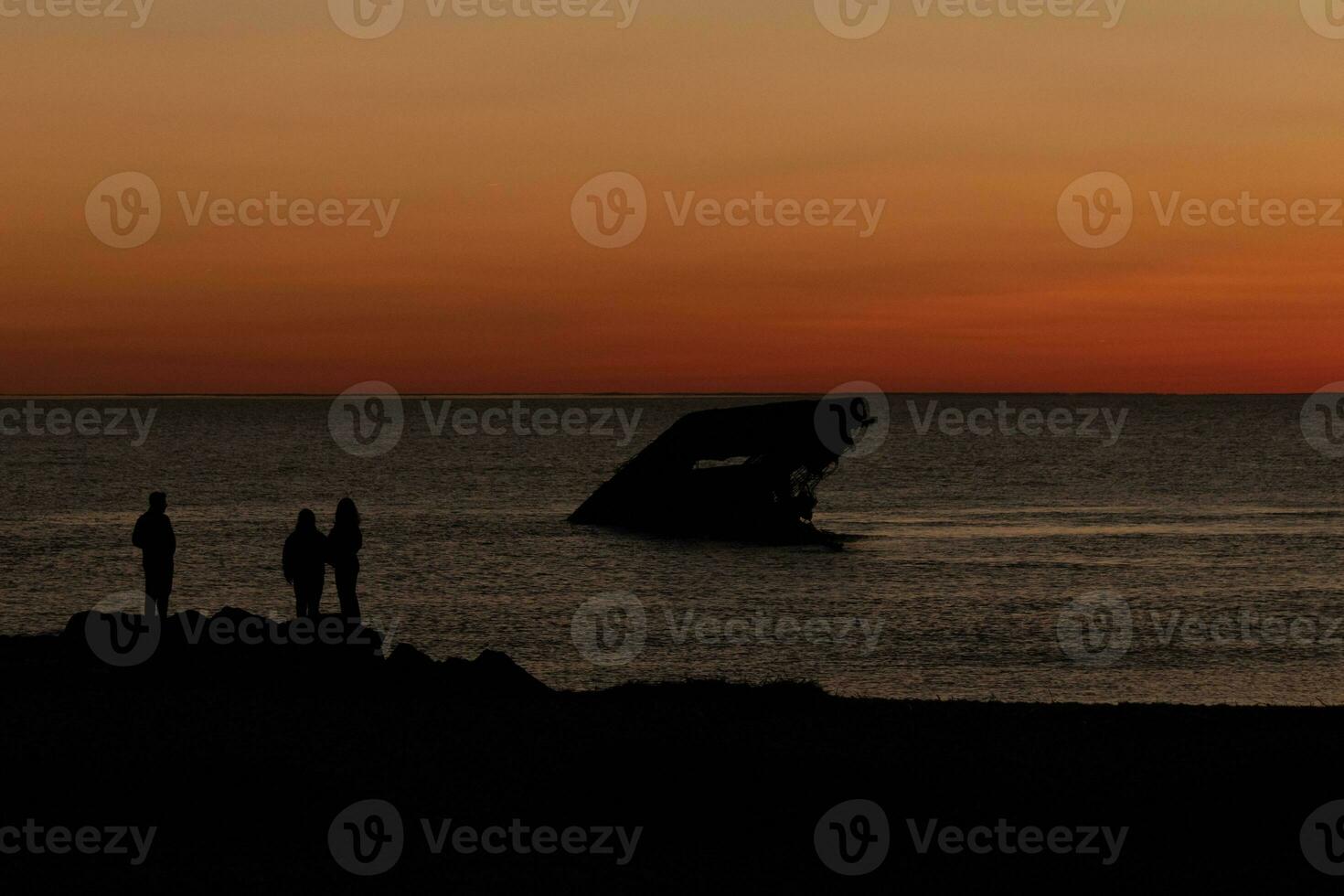 Sol configuração em a Delaware baía. a bonita vermelho cores gostar a céu é em fogo. a afundado navio do capa pode sentado dentro a oceano. pessoas em pé em a ampla Preto pedras do a cais do a de praia. foto