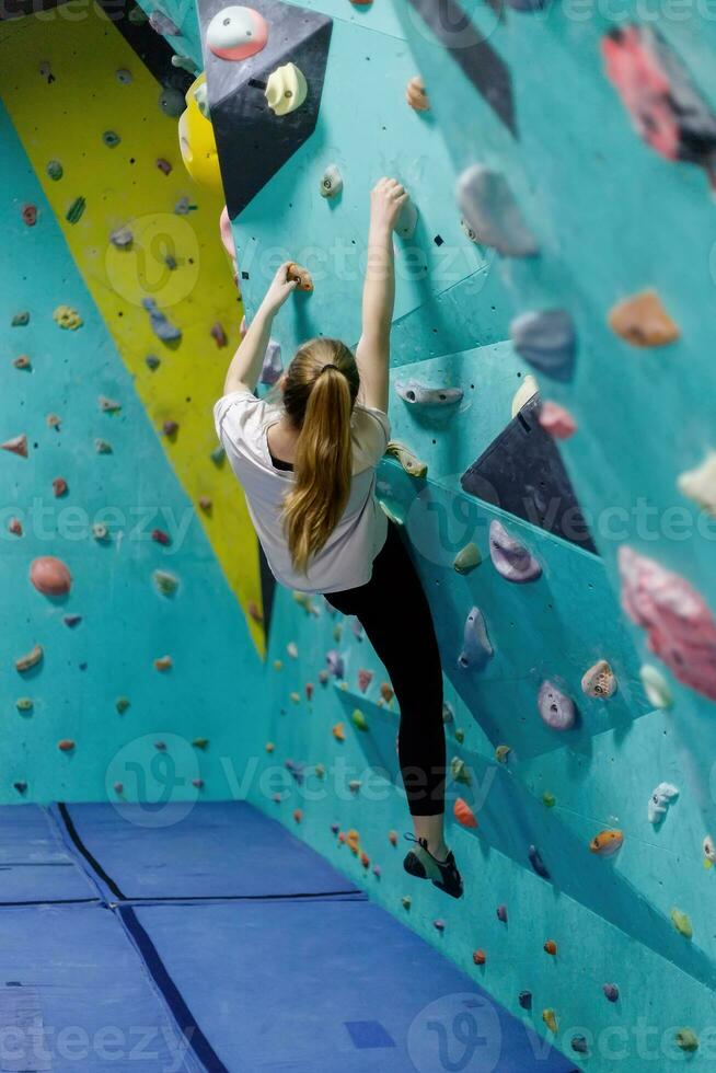 jovem mulher escalada acima em prática parede dentro Academia foto