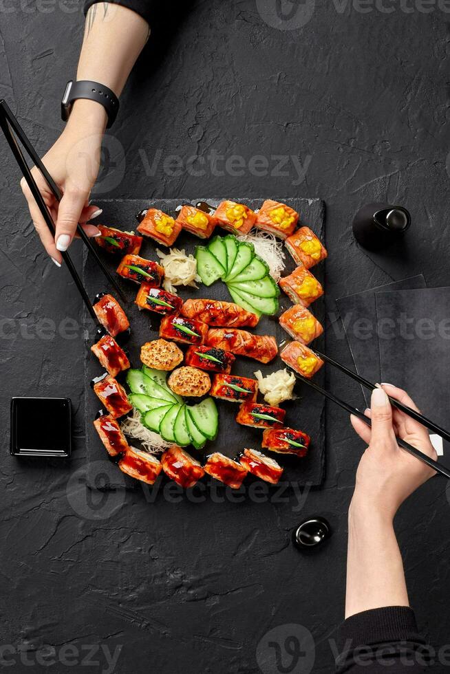 dois fêmea mãos usando pauzinhos para levar rolos a partir de Sushi conjunto foto