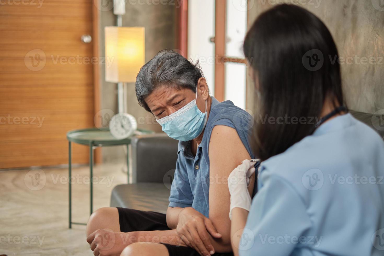 uma médica asiática está vacinando um homem idoso em casa. foto