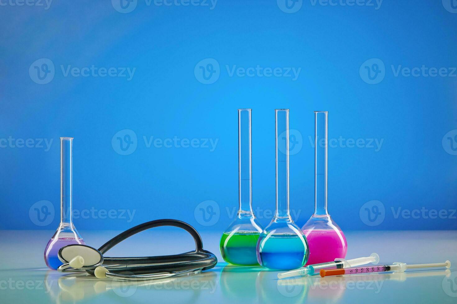 quatro médico frascos com colorida químico reagentes. teste kit, seringa e estetoscópio, azul fundo. coronavírus. pandemia COVID-19. fechar acima foto