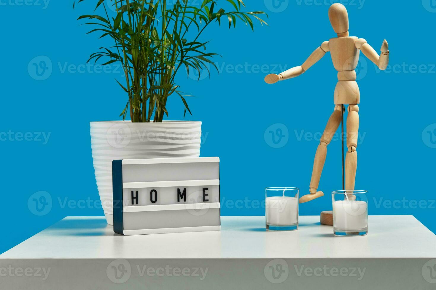 branco café mesa com verde flor dentro Panela, dois velas, de madeira estatueta do humano e decoração elemento com inscrição lar. azul fundo. fechar acima foto