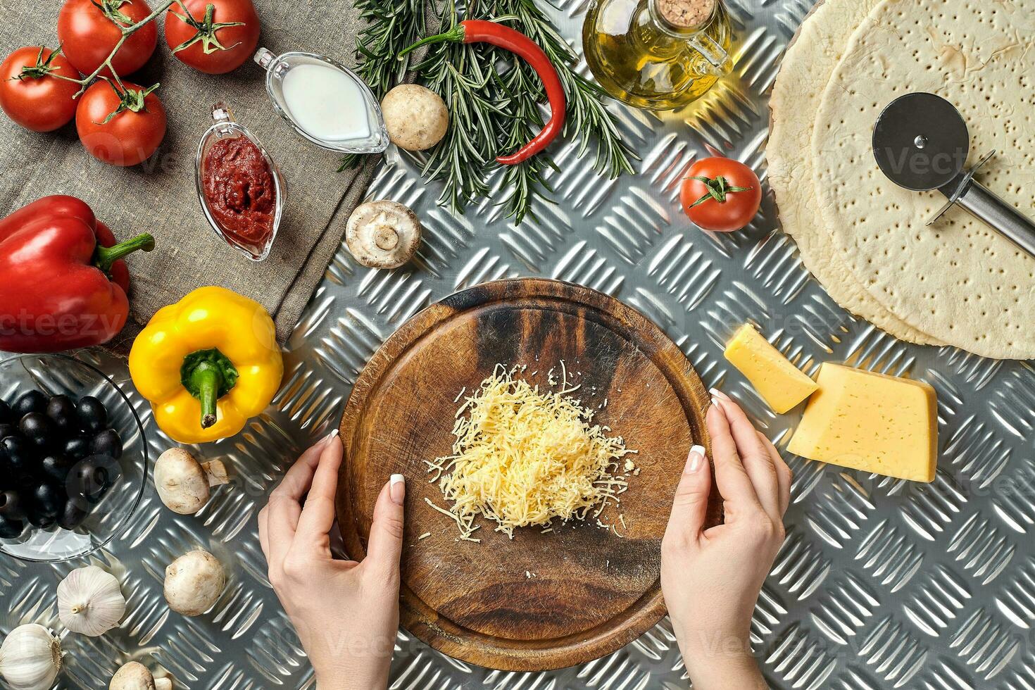 fêmea mãos esfregou queijo Grato em pizza, ingredientes para cozinhando pizza em metal mesa, topo Visão foto