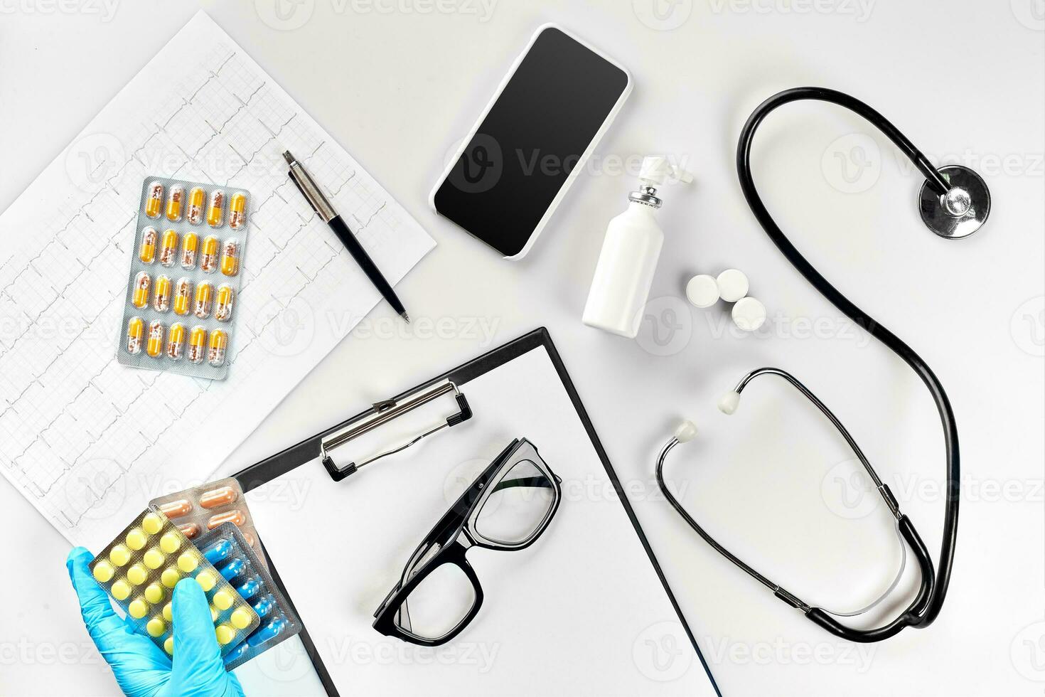 local de trabalho do uma doutor. pílulas dentro mão, estetoscópio, prancheta e óculos em branco mesa foto