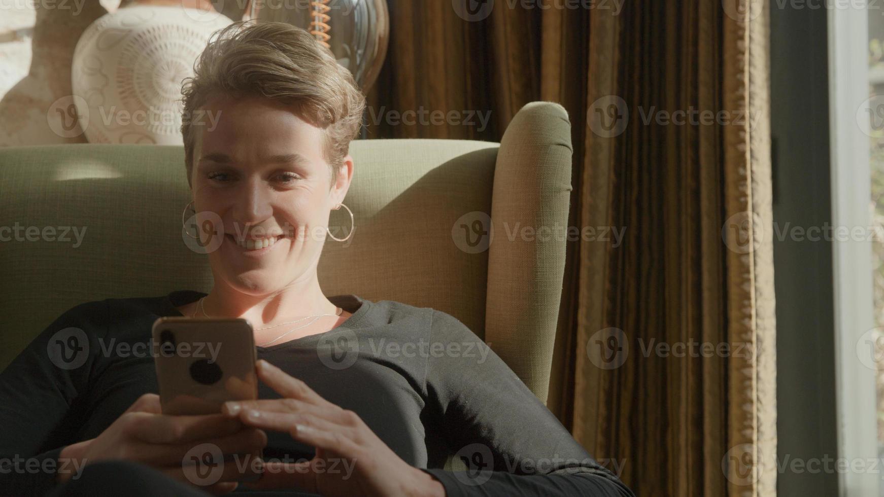 mulher na poltrona segurando smartphone e rindo foto
