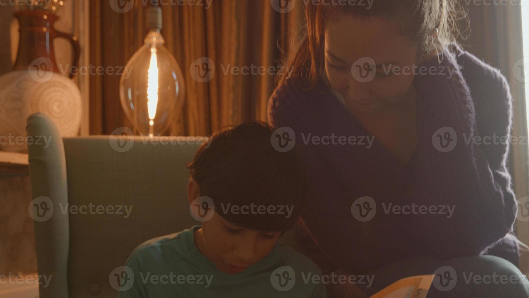 mulher juntando-se ao menino fazendo lição de casa na poltrona foto